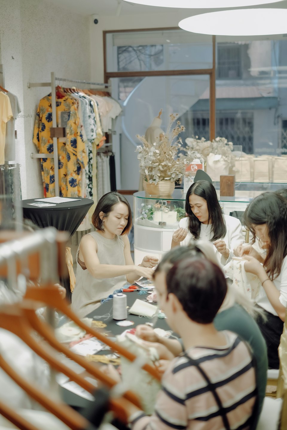 Women work on embroidery projects around a table at a shop.