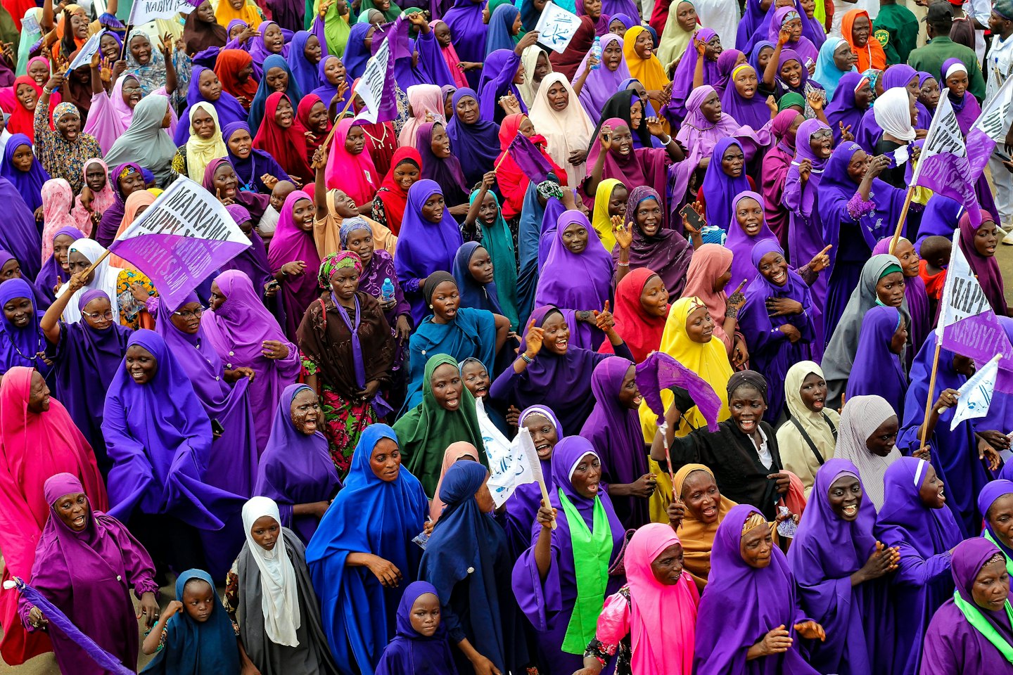 A group of women and girls in colorful hijabs waving flags.