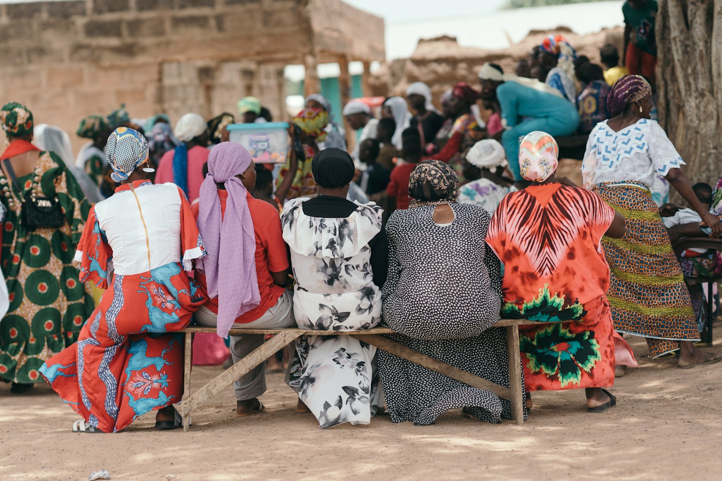 Women in traditional clothing sit on a wooden bench outdoors.