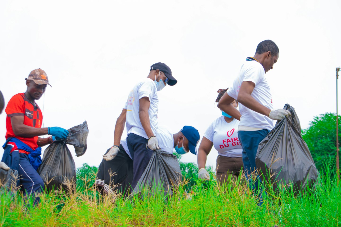 Five volunteers collect trash from an overgrown grassy field.