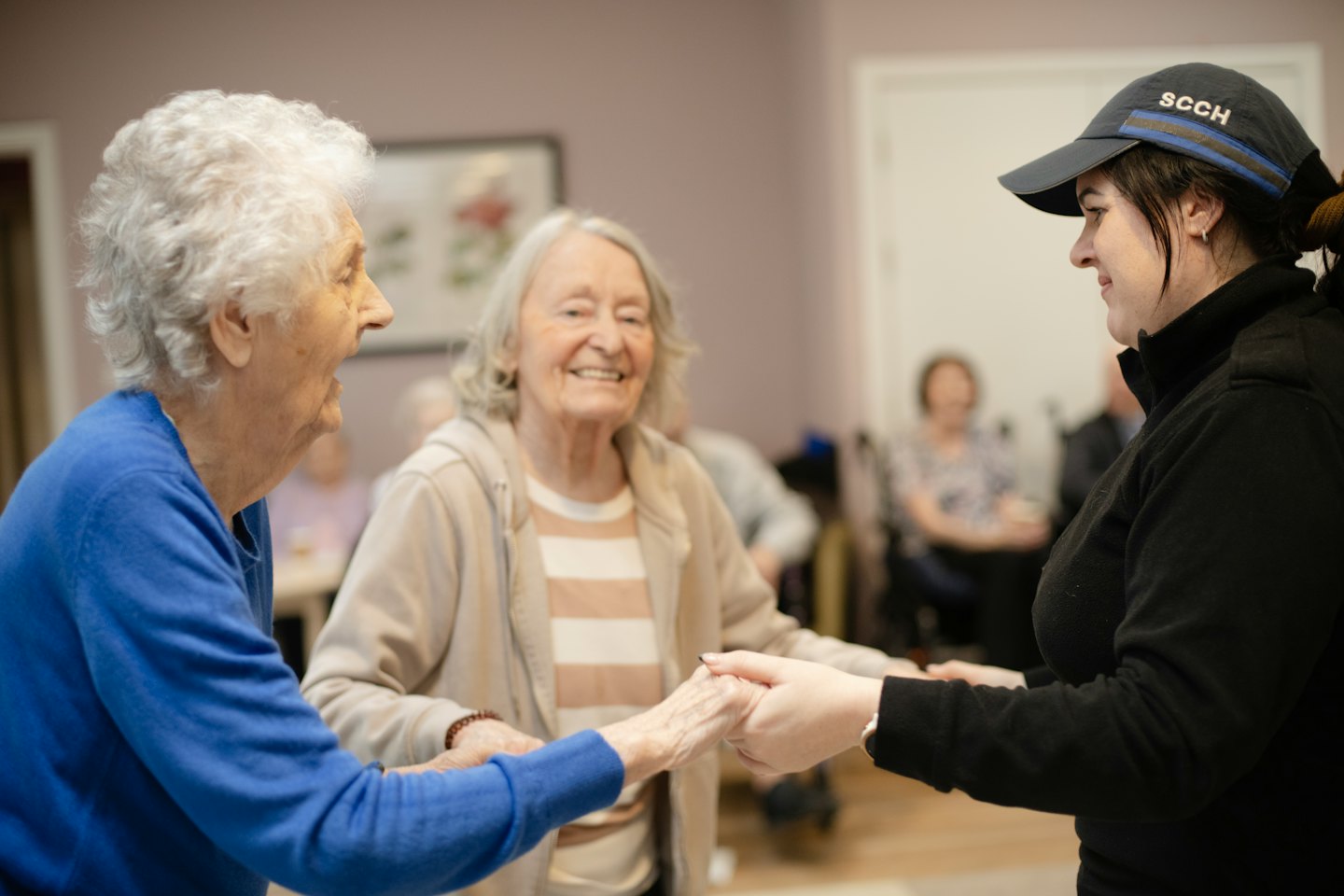 Three smiling women hold hands during an indoor group activity.